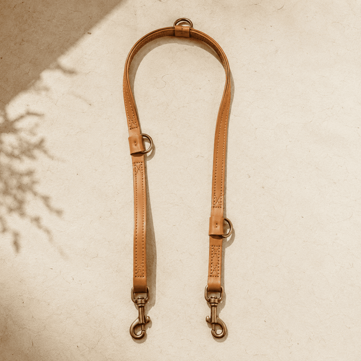 An adjustable leather lead with two brass snaps and three rings shown at its longest setting