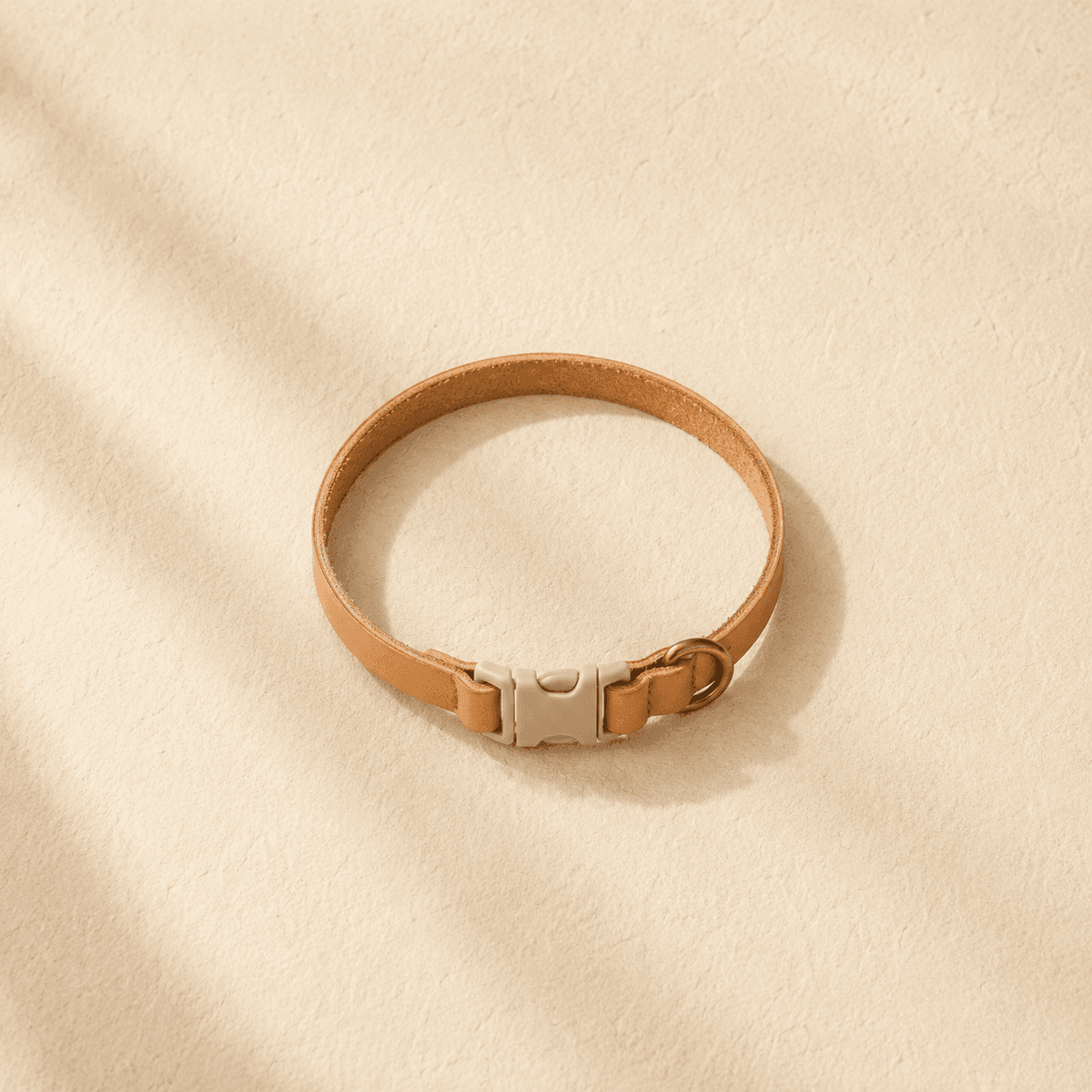A narrow 10 mm light tan cat collar with a breakaway buckle and small brass tag ring