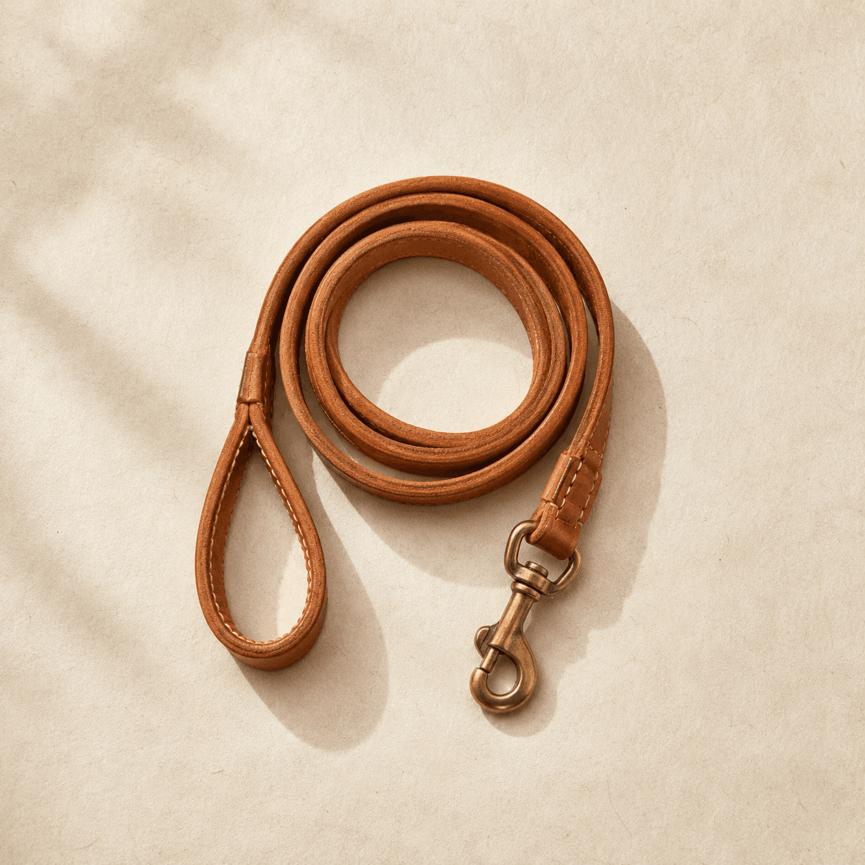 A 120 cm tan leather dog lead with a brass swivel snap, coiled on a cream surface