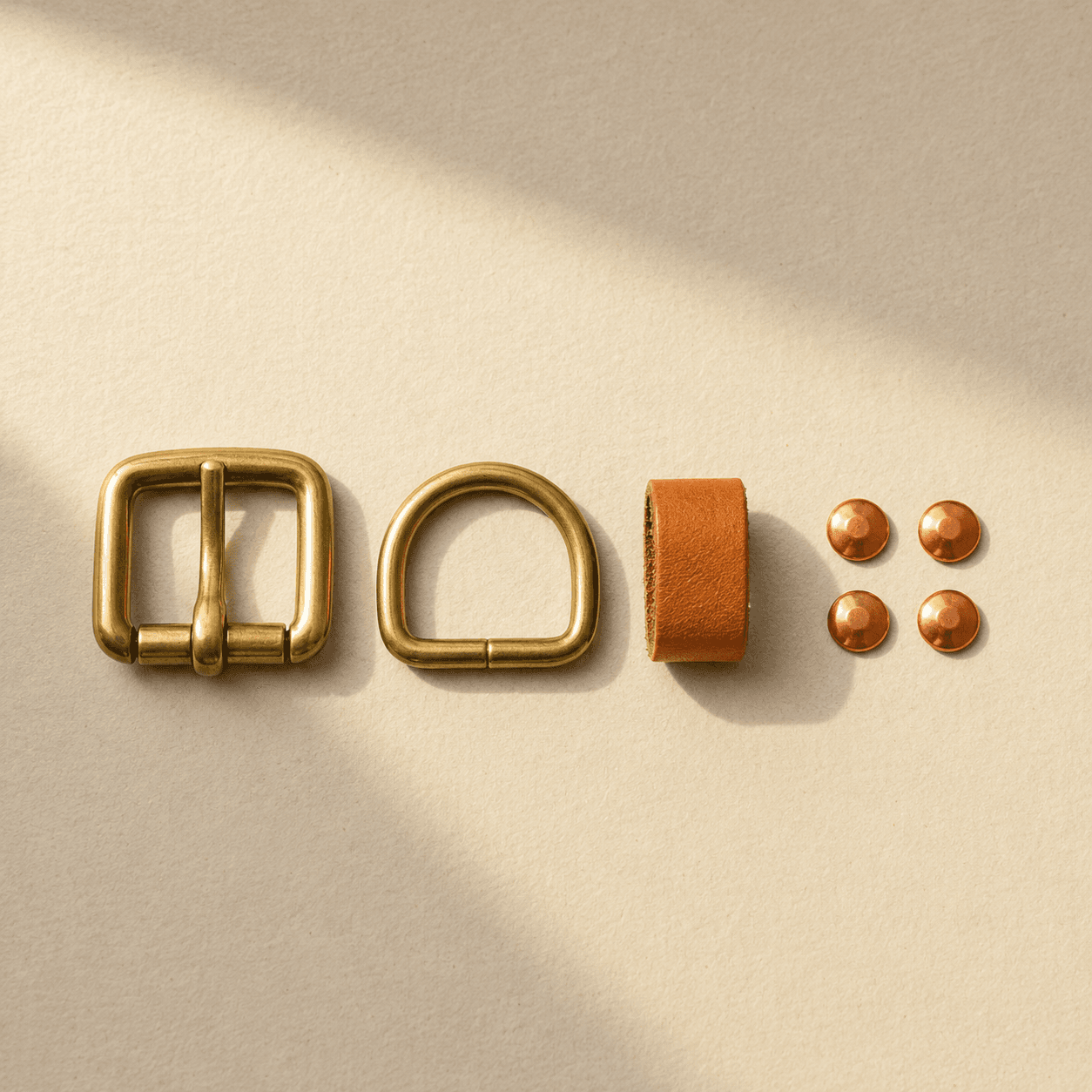 A brass buckle, D-ring, leather keeper and four copper rivets arranged on cream paper