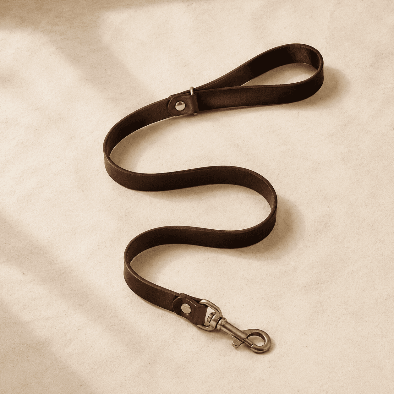 A 180 cm dark brown leather lead with brass fittings laid in a loose S-shape